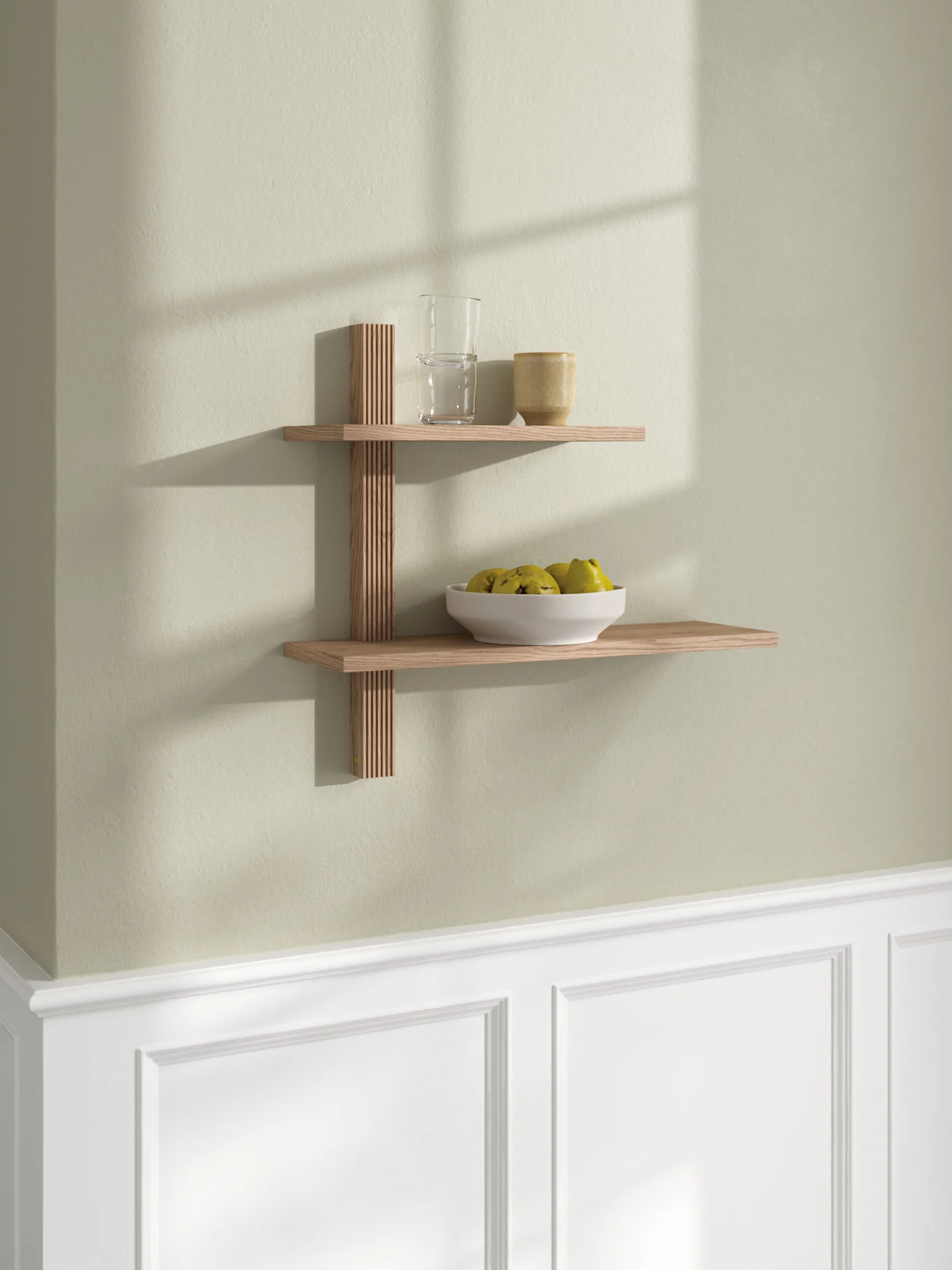 Zweistöckiges Wandregal aus Holz mit Lamellenstütze, darauf ein Glas, eine Tasse und eine Schale mit gelb-grünem Obst.
