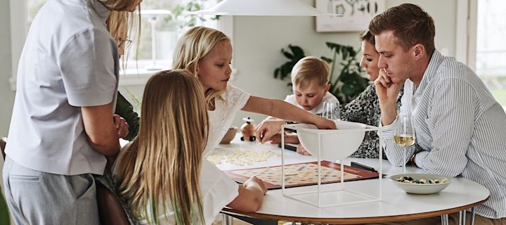 Die Familie versammelt sich um den Tisch und spielt gemütlich Gesellschaftsspiele in einer hyggeligen Atmosphäre.