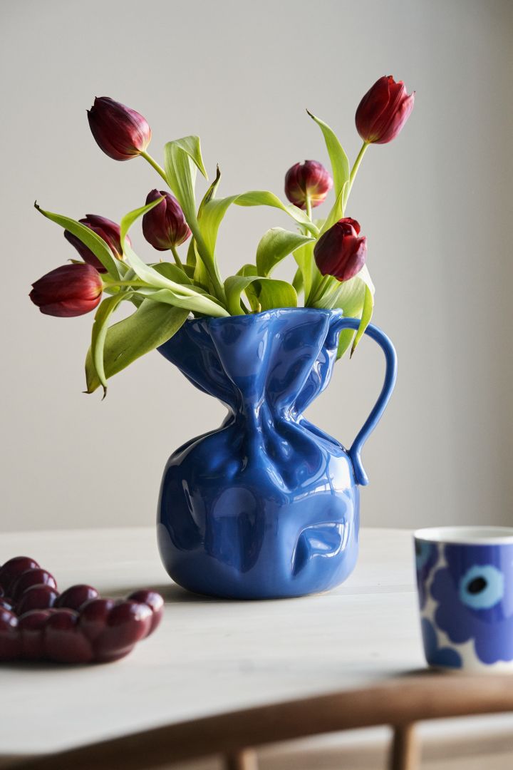 Folgen Sie den Wohntrends für den Herbst 2023 und setzen Sie kornblumenblaue Akzente in Ihrem Interieur - hier die Vase Crumble von By On mit roten Tulpen. 