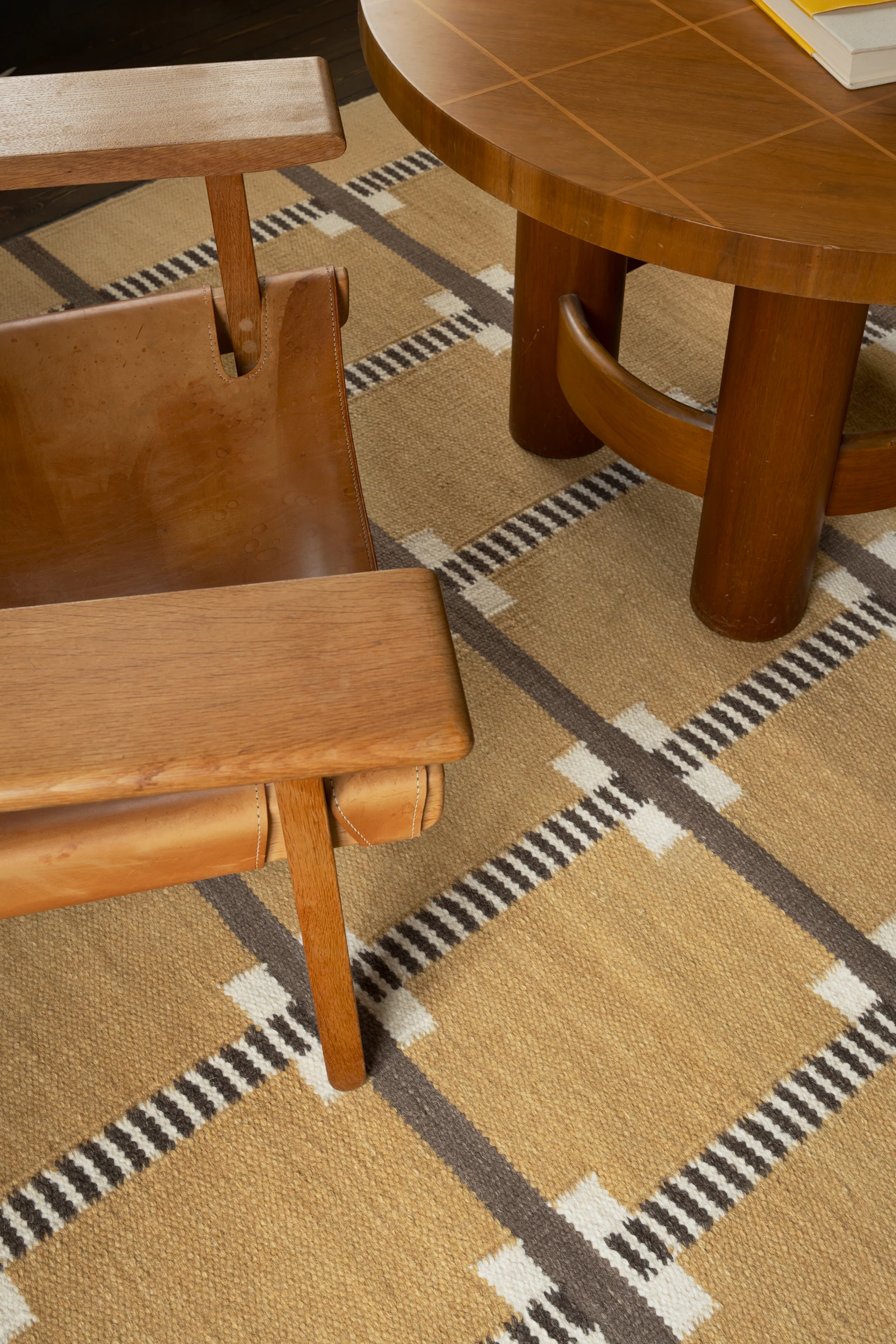 Holz-Sessel mit Ledersitz neben einem runden Couchtisch auf einem geometrisch gemusterten Teppich.