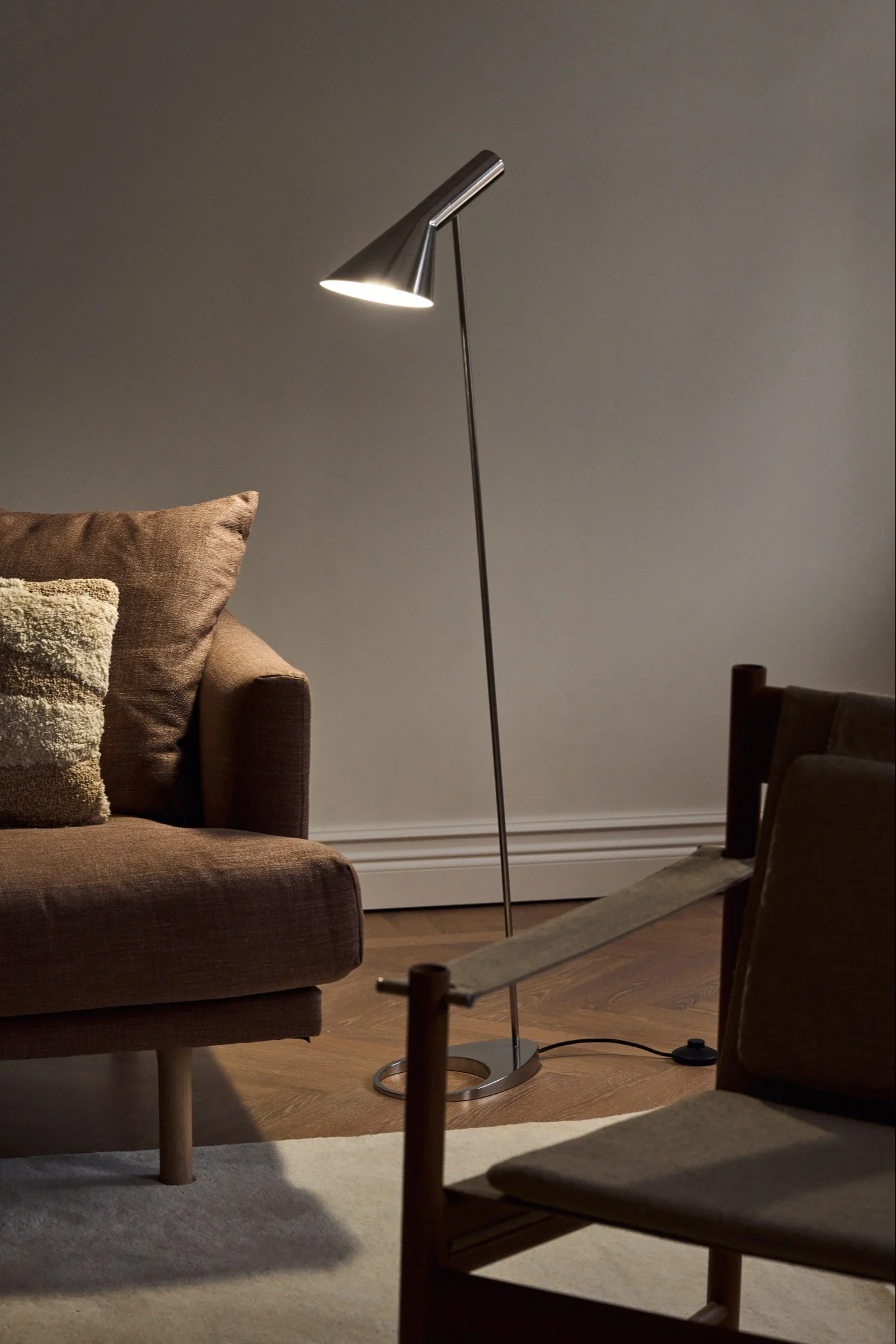 Skandinavische Lampen: Die chromfarbene AJ-Stehlampe von Louis Poulsen steht in einem schlichten Wohnzimmer neben einer Couch.
