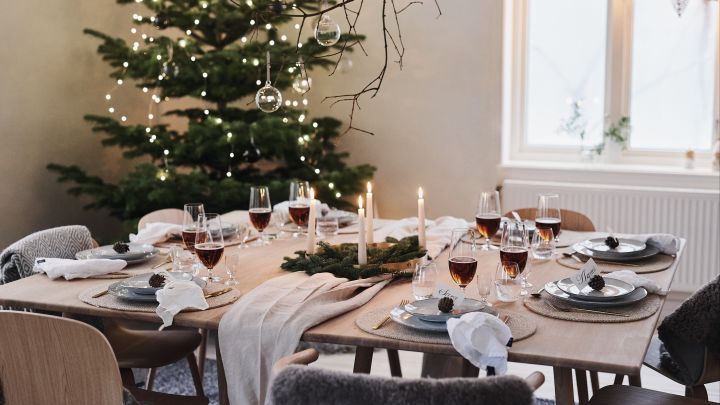 Ein weißes und minimalistisches Weihnachtsgedeck beim diesjährige Weihnachtsessen mit natürlichen Dekorationen wie Zapfen und Tannenzapfen auf dem gedeckten Tisch.
