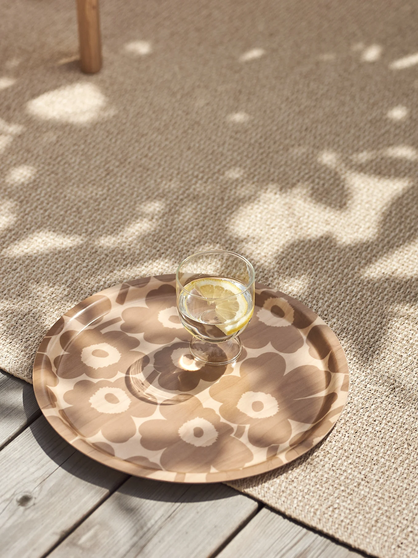 Glas Zitronenwasser auf einem beigen, blumengemusterten Tablett auf einem strukturierten Teppich mit gesprenkeltem Sonnenlicht.