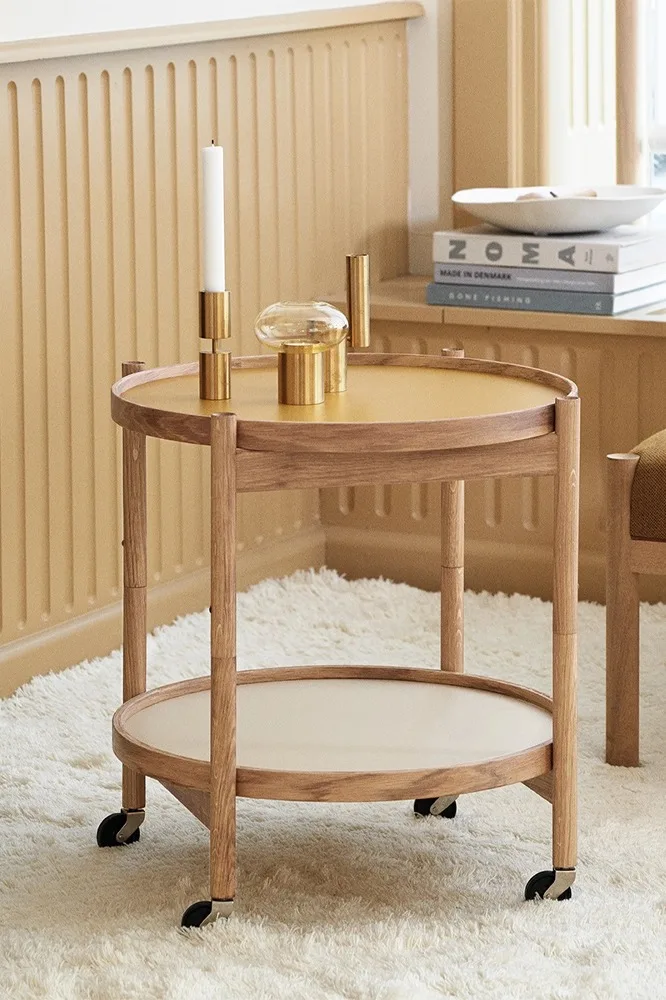 Runder, zweistufiger Servierwagen aus Holz mit senfgelber Platte und Messingdekorationen auf einem cremefarbenen Zottelteppich.