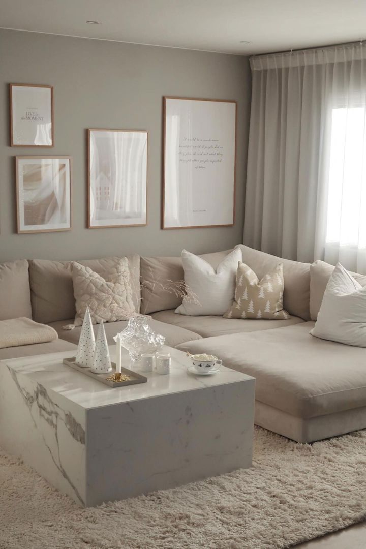 Das beige Wohnzimmer von @casa_pedersen mit einem marmornen Couchtisch, einer beigen Couch, hellem Teppich, beigefarbenen Kissen und Bildern an den Wänden.