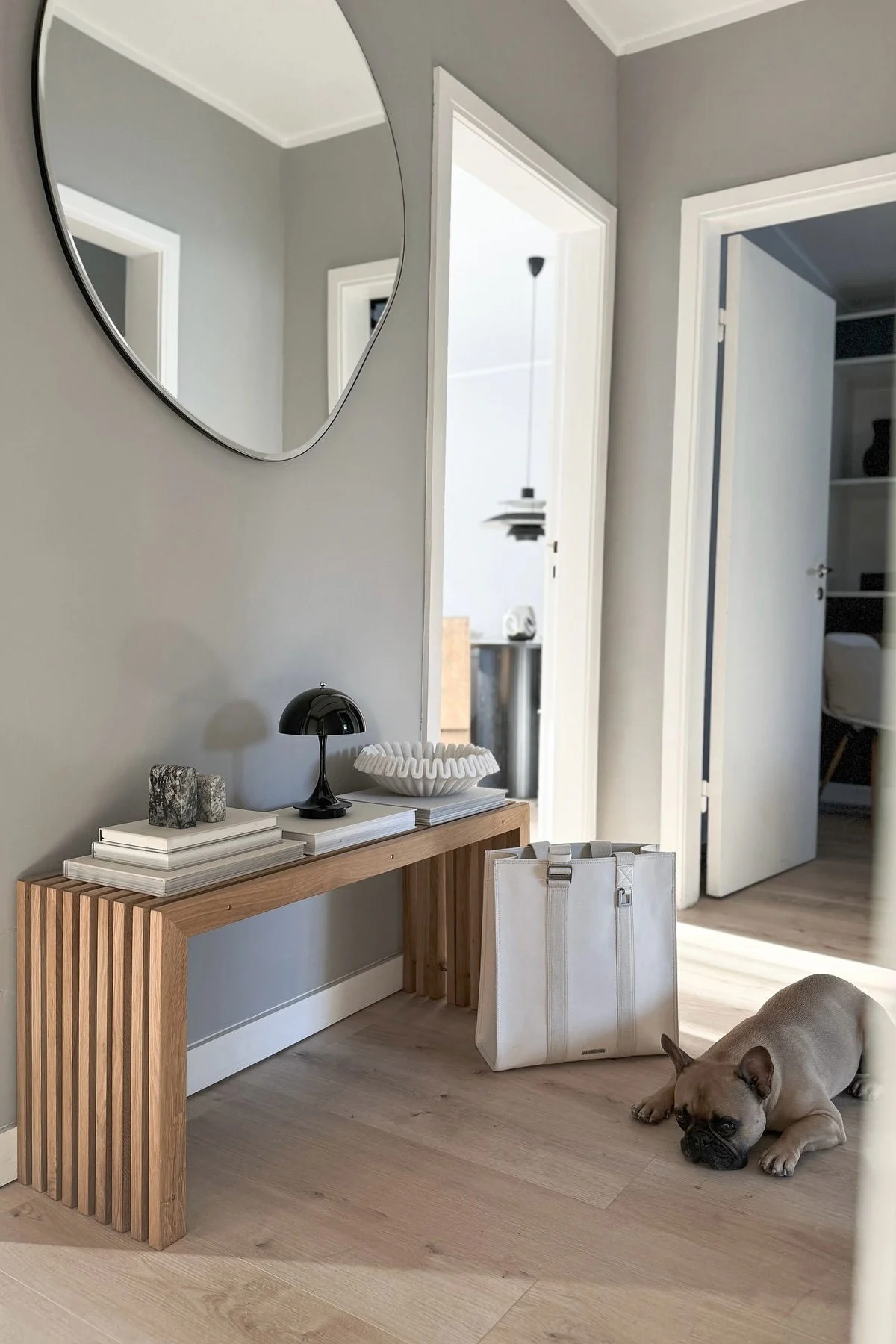 Der einheitlich gestaltete Flur von @alexander.stoeckel mit dem Pond Spiegel von Ferm Living, der Panthella Tischleuchte auf einer Bank und einem Hund.