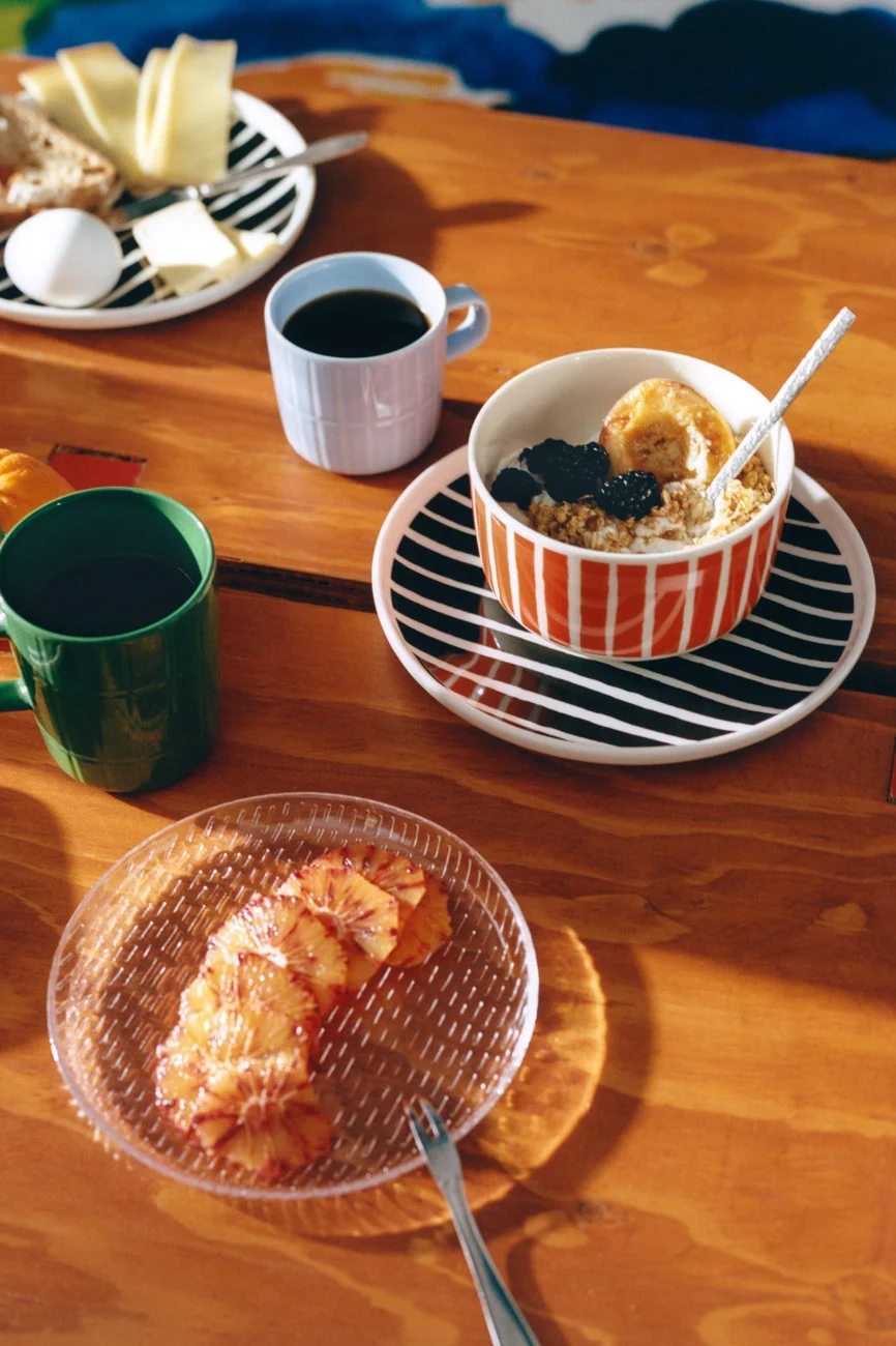 Frühstück auf Holztisch mit gestreiften Geschirr, Kaffee, Haferbrei, Käse, Brot, Ei und Blutorangenscheiben.