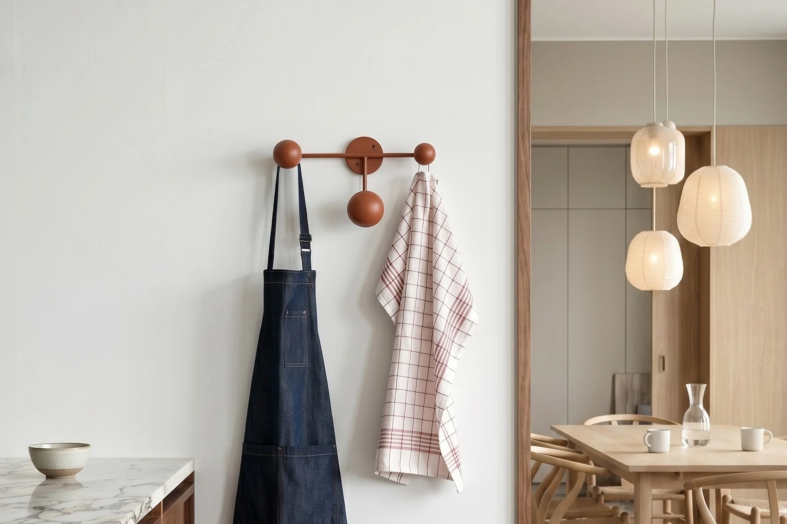 Küche mit Marmor. Blaue Schürze, kariertes Geschirrtuch an Garderobe. Esszimmer mit Tisch und Pendelleuchten.