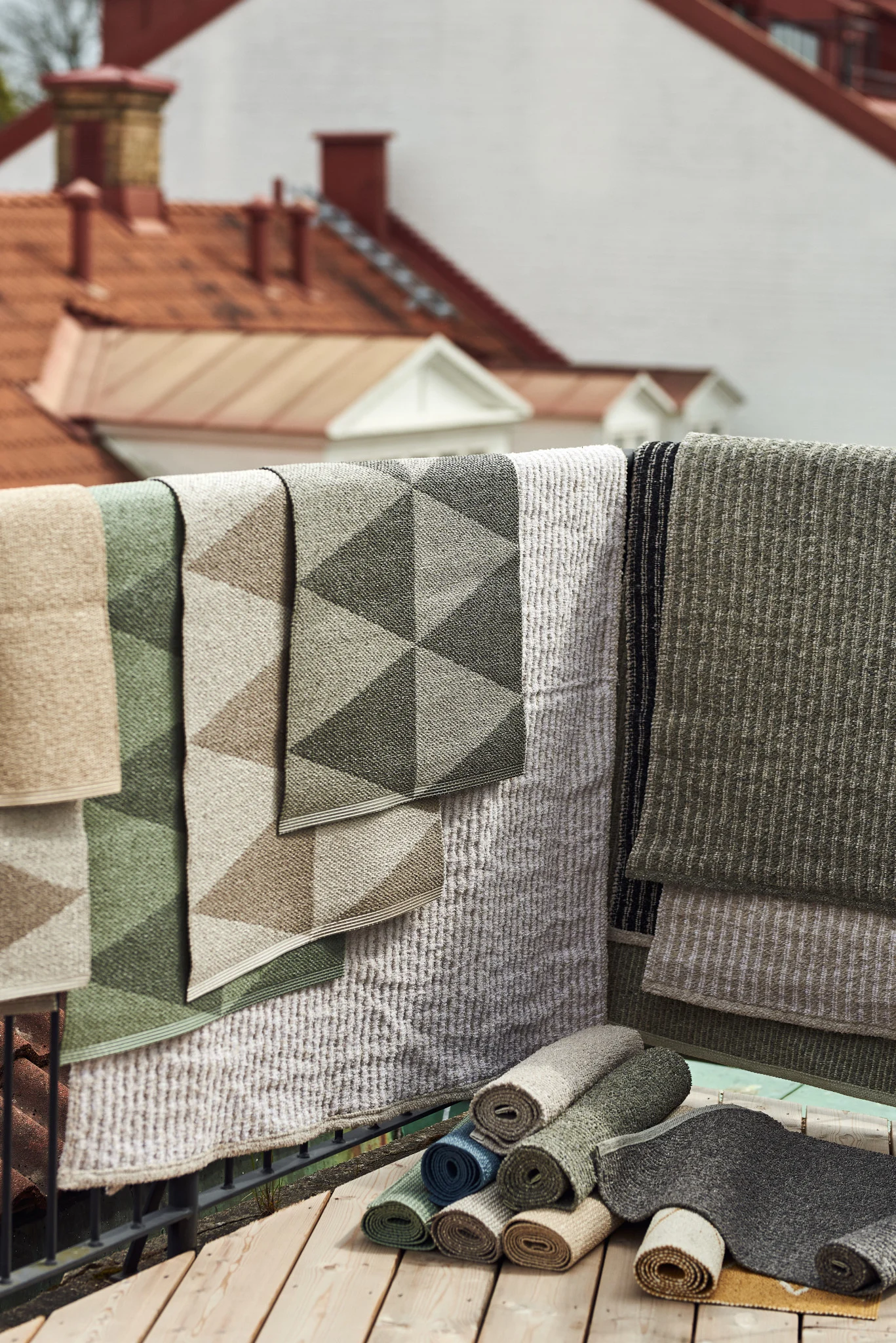 Outdoor Teppich: Hier sehen Sie die zahlreichen Outdoor-Teppiche von Scandi Living in verschiedenen Größen, Materialien und Farben über einem Balkongeländer hängen.