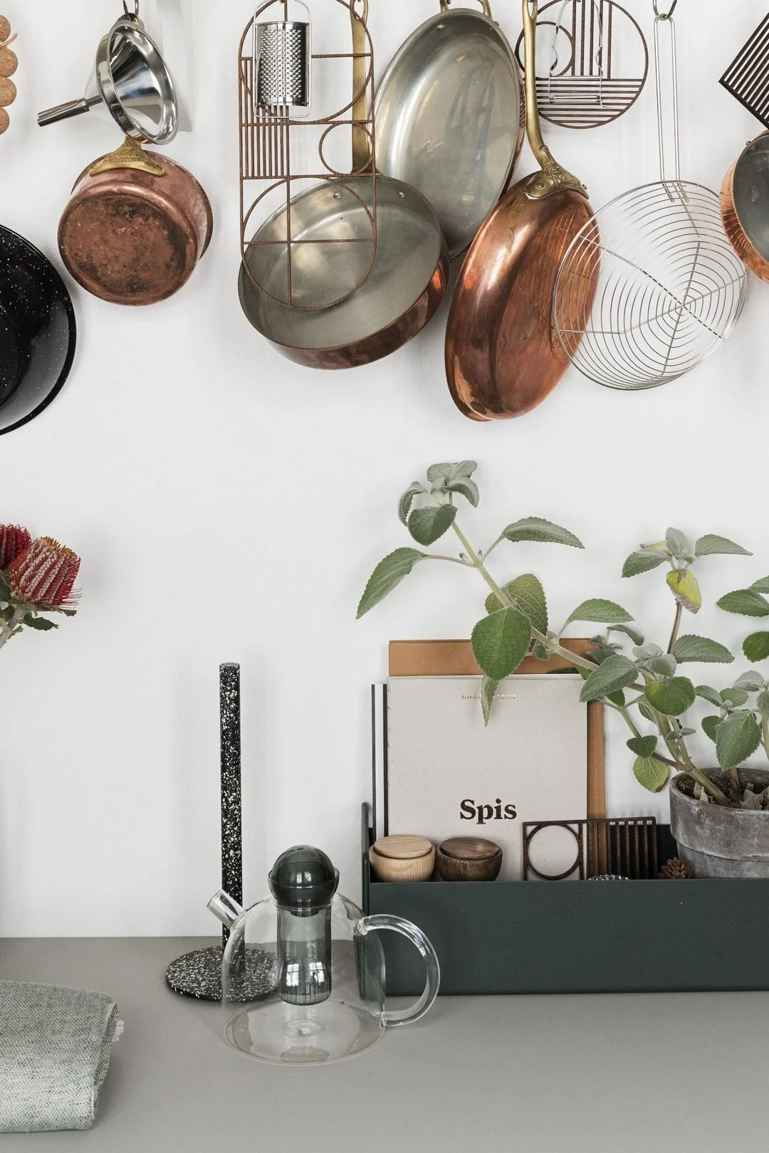 Die Still Teekanne von Ferm Living ist schlicht, aber stilvoll und steht hier auf einer Küchentheke, darüber hängen Pfannen.