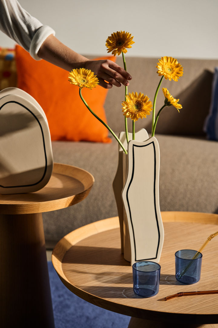 Bei den skandinavischen Wohntrends 2024 sehen wir viele verspielte Formen mit Retro-Vibes. Hier: Eine schwarz-weiße Vase von ferm Living mit gelben Blumen.