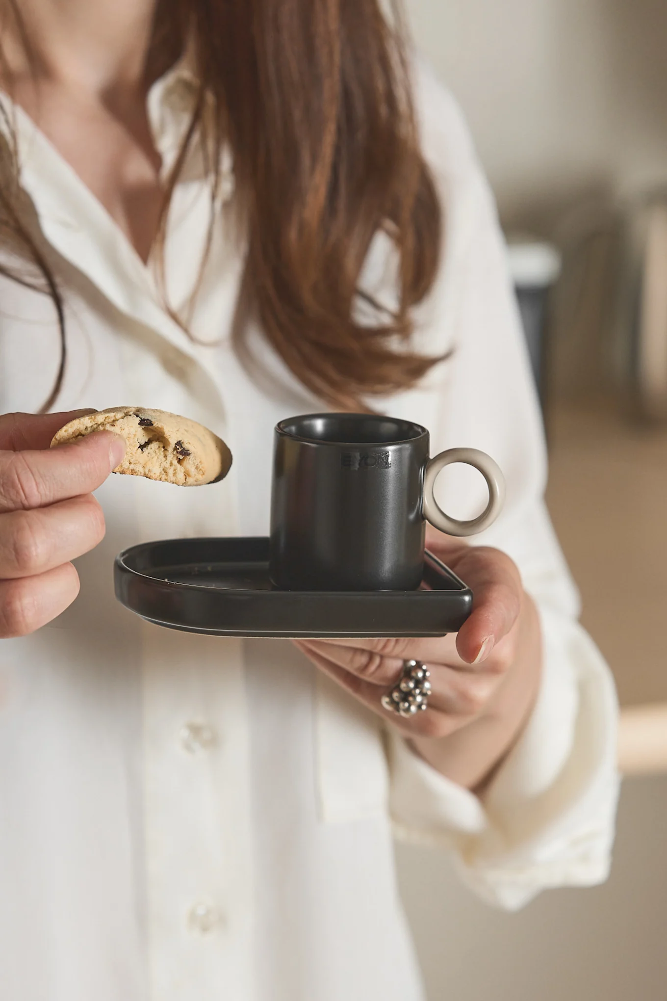 Hier sehen Sie eine Frau, welche in der einen Hand die Niki Espressotasse von Byon hält und in der anderen einen Biscotti.