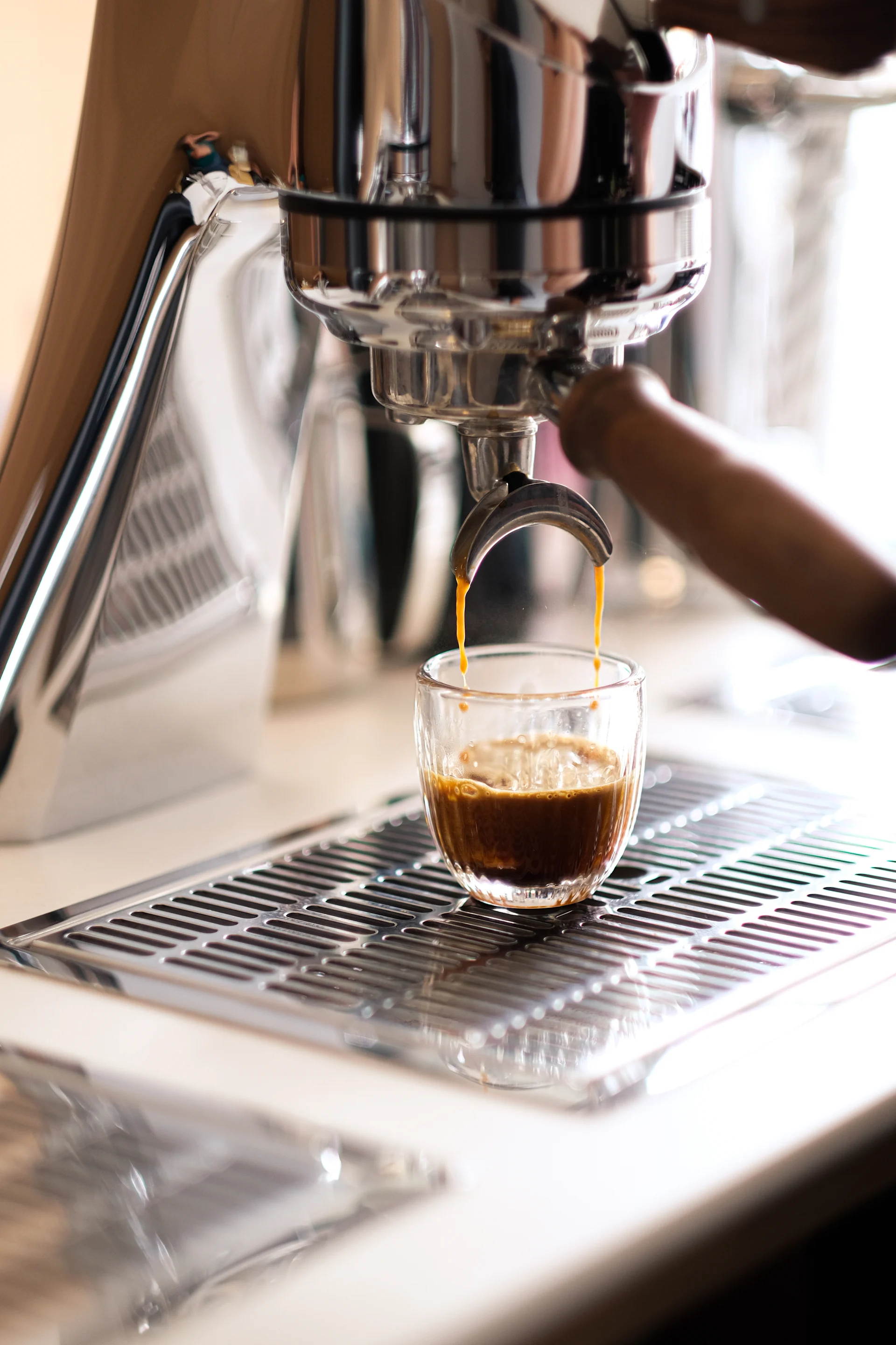 Espressomaschine gießt frischen Kaffee in eine Glastasse auf einem Metallrost.