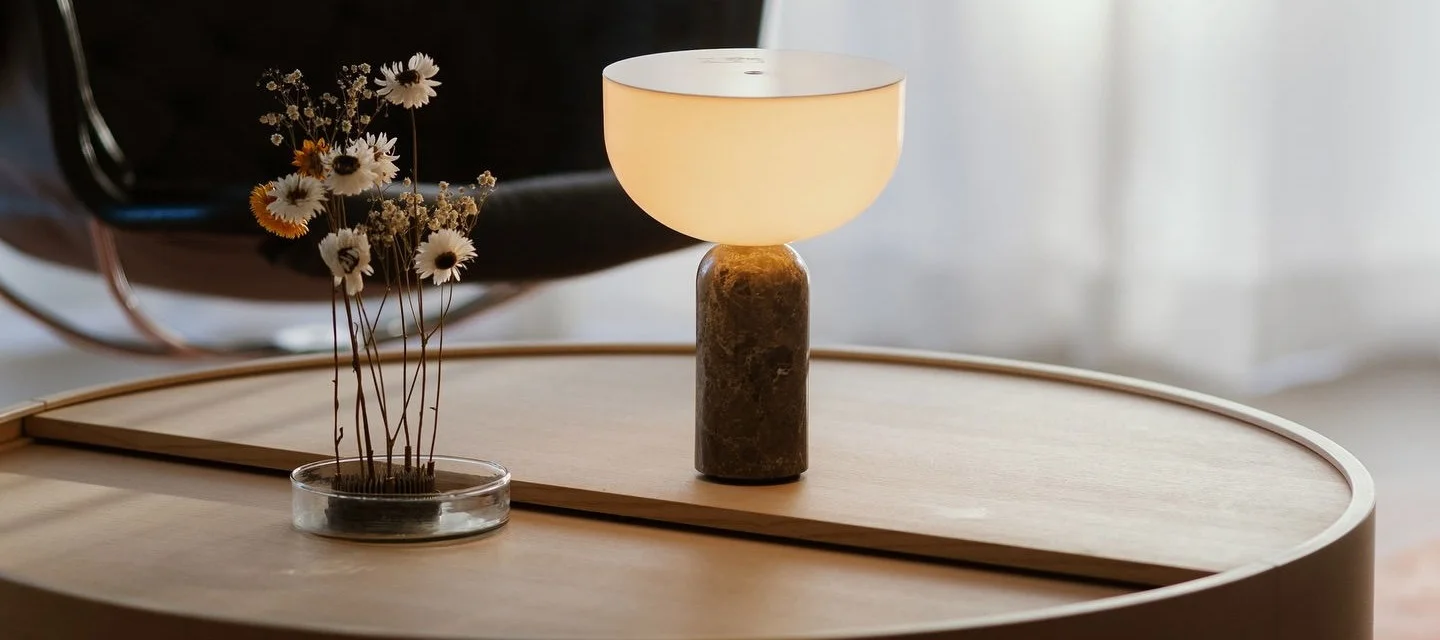Der Arc Couchtisch von Woud ist dekoriert mit einer Kizu Tischleuchte von New Works und dem Garden Glory Blumenigel.