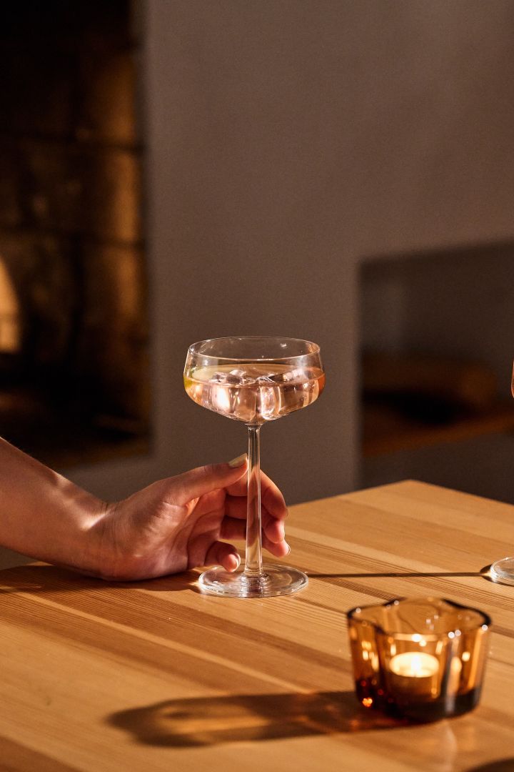 Geschenkideen zu Weihnachten: Hier sehen Sie ein gefülltes Cocktailglas aus der Essence-Kollektion von Iittala auf einem Holztisch stehen.
