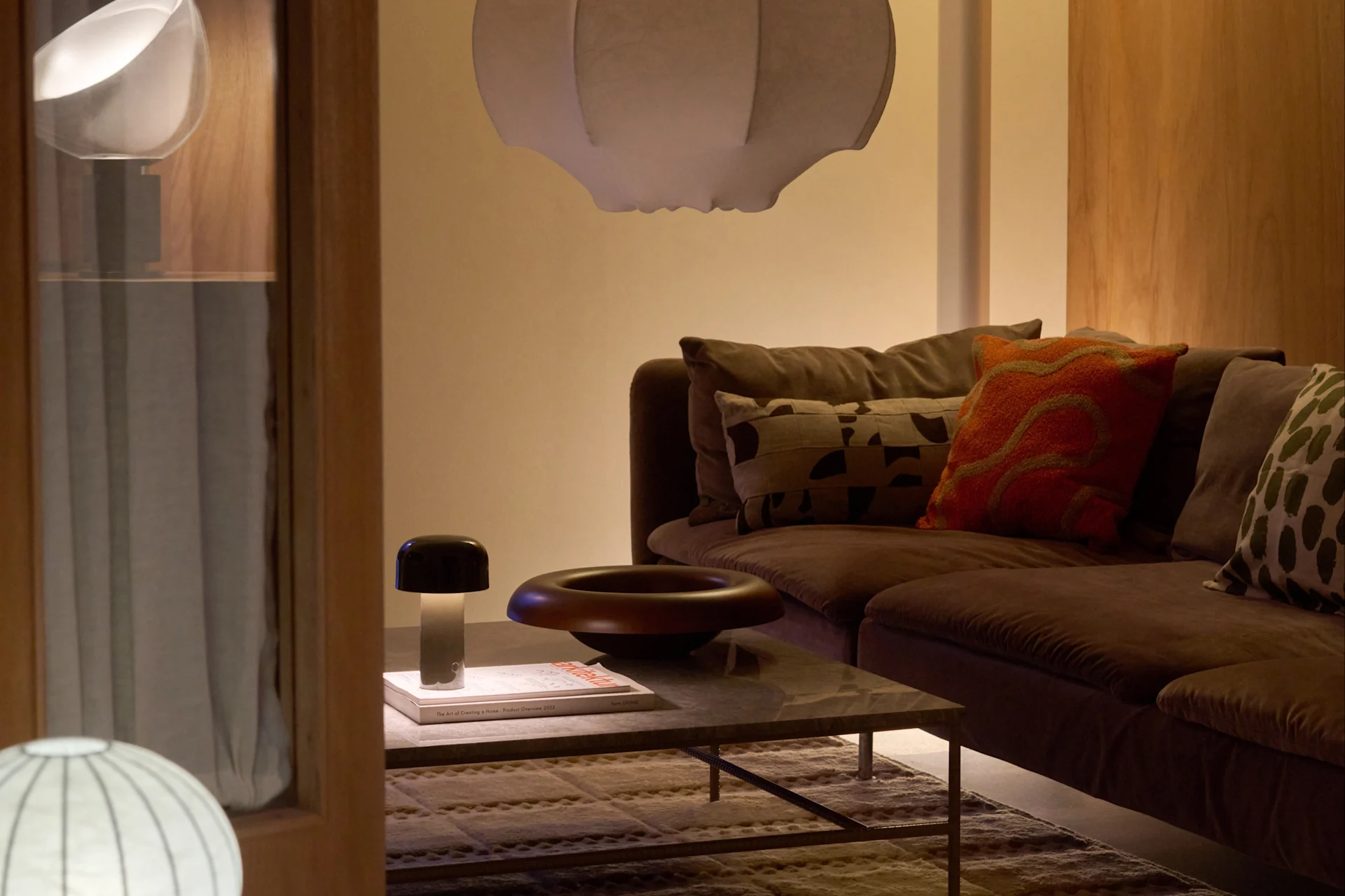 Gemütliches Wohnzimmer mit braunem Sofa, weißer Hängelampe, Stehlampe und Couchtisch mit Pilzlampe und Dekoschale.
