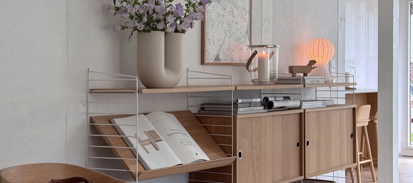 Modulares Regalsystem mit weißen Rahmen, Holzregalen, Schränken, Vase mit lila Blumen, Laterne und leuchtender Pilzlampe.