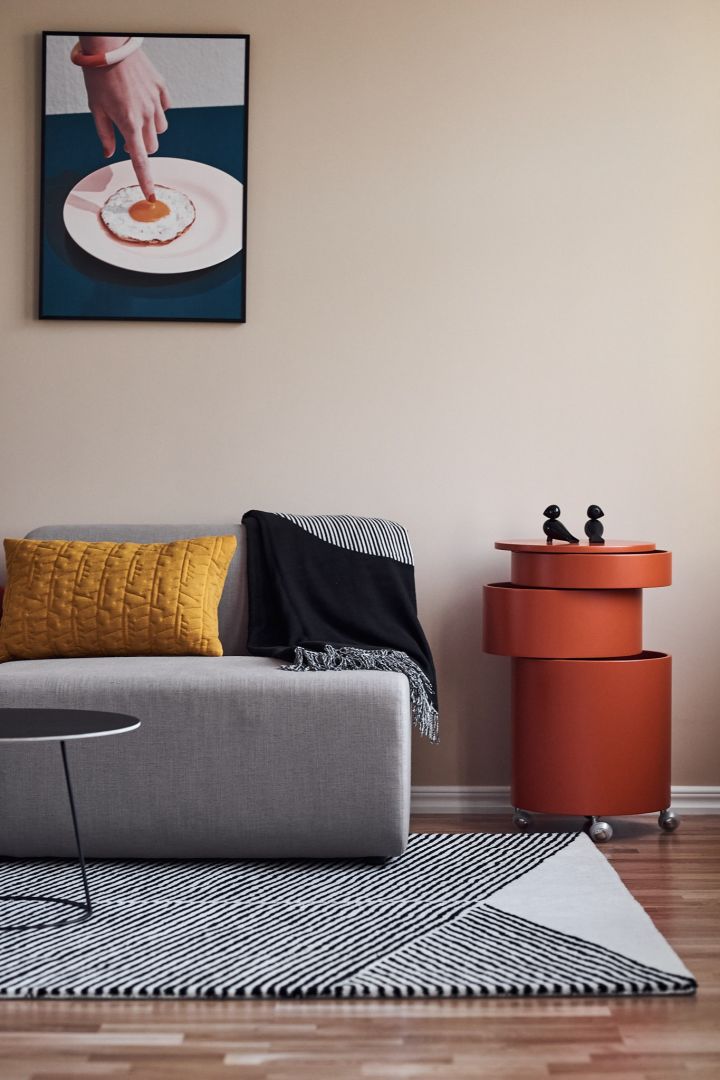 Colourblocking ist ein beliebter Farbtrend 2022 – hier in einem Wohnzimmer mit schwarz-weißem Teppich von NJRD, gelbem Kissen und rotem Servierwagen.