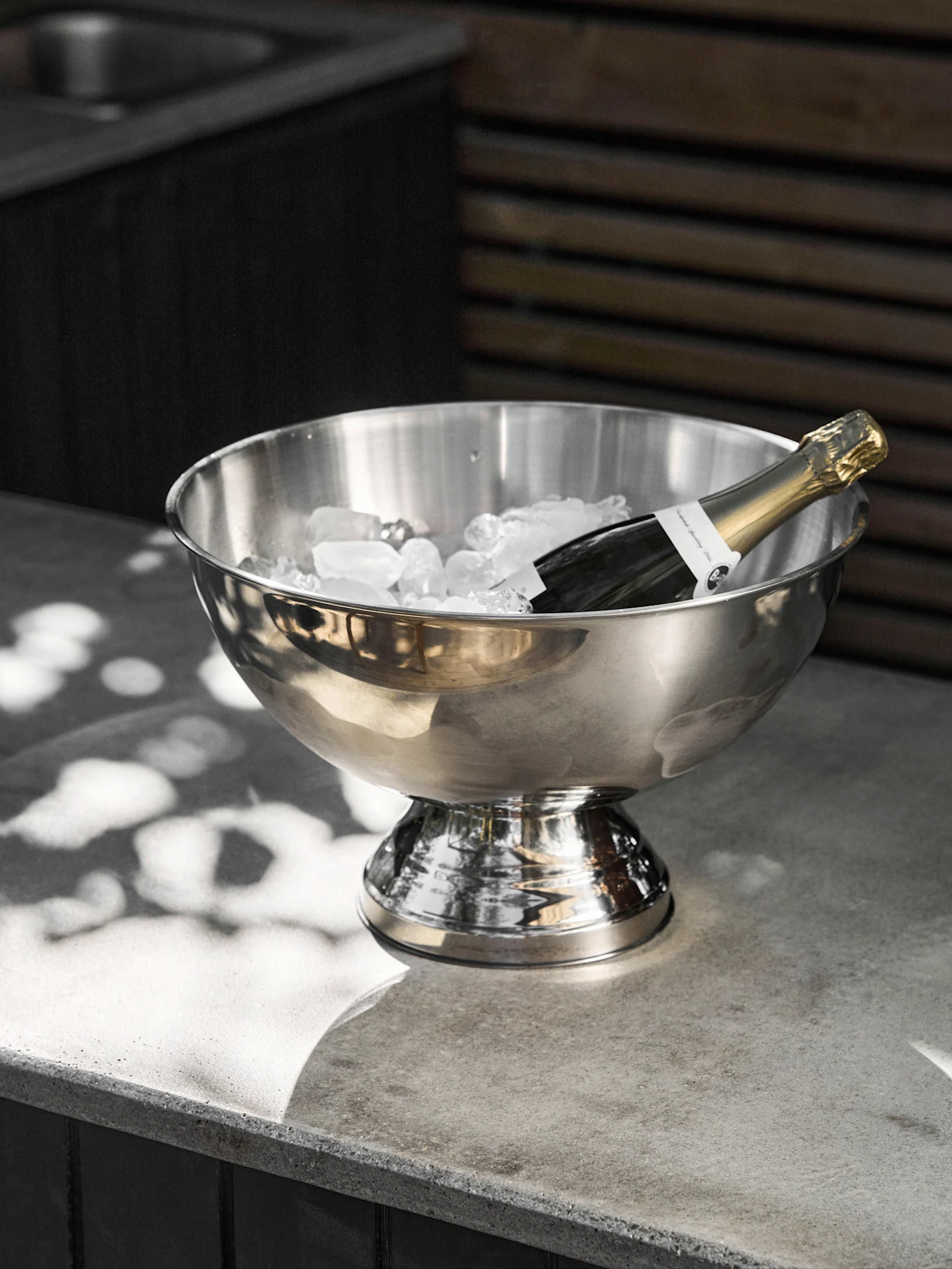 Champagnerflasche kühlt in einem Eisbehälter aus Edelstahl auf Betonoberfläche.