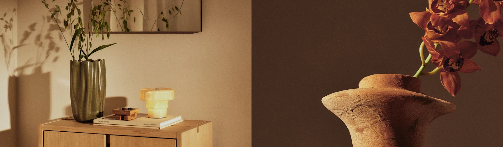 Zwei Vasen präsentieren Pflanzen, eine grüne Vase mit Blattwerk auf einem Schrank neben einer gelben Lampe und eine Terrakottavase mit orangefarbenen Orchideen.