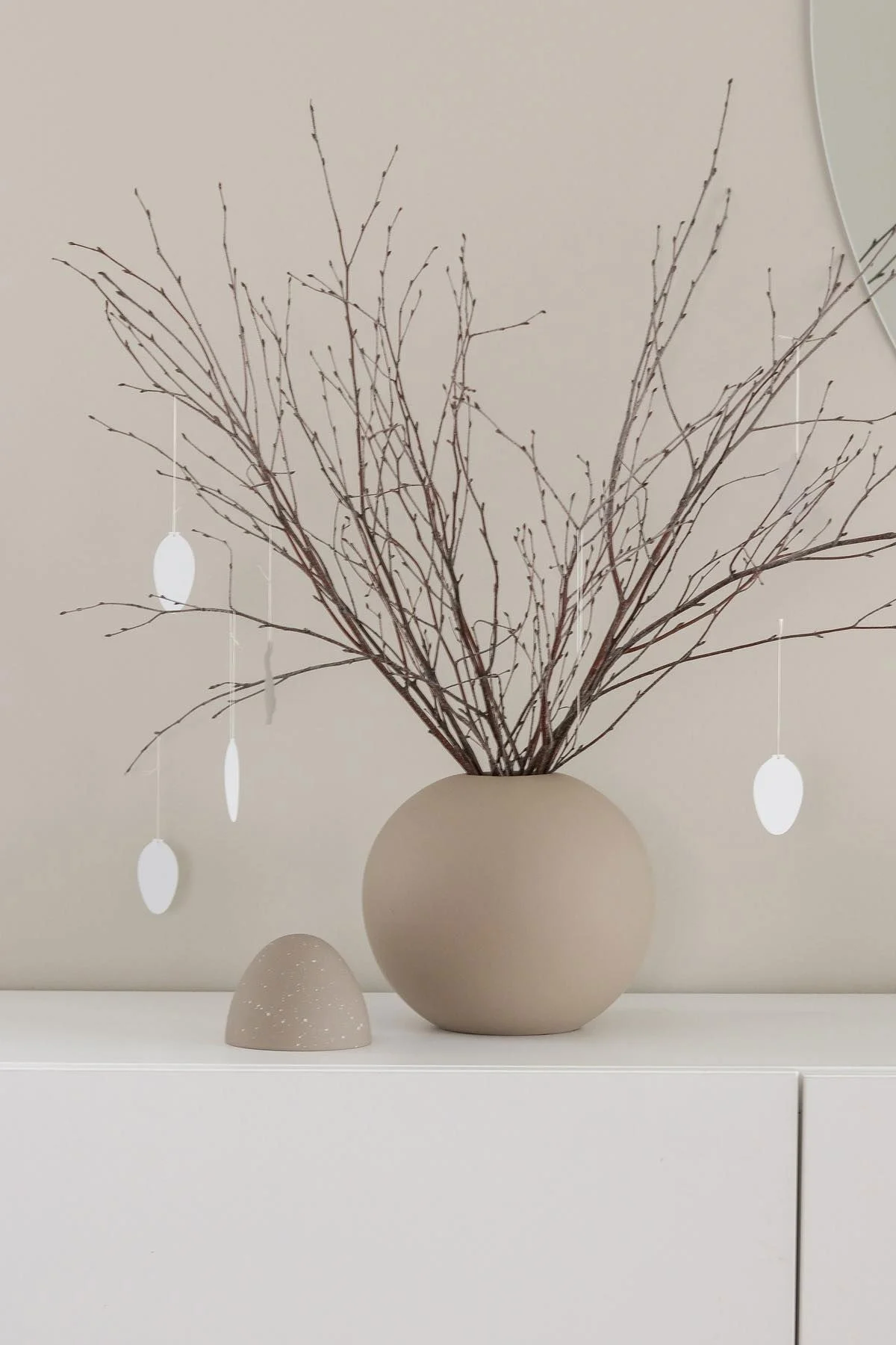 Ein Osterstrauch steht auch einer weißen Kommode in einer sandfarbenen Ball Vase mit Easter Deco Ei-Anhängern, beides von Cooee Design, im Zuhause von @tunadalen.