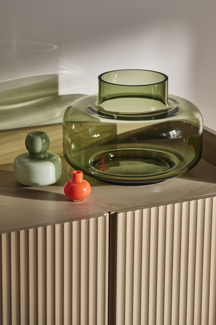 Die Urna-Vase in Grün von Marimekko steht zusammen mit der Mini-Vase in Orange auf einem Schrank.