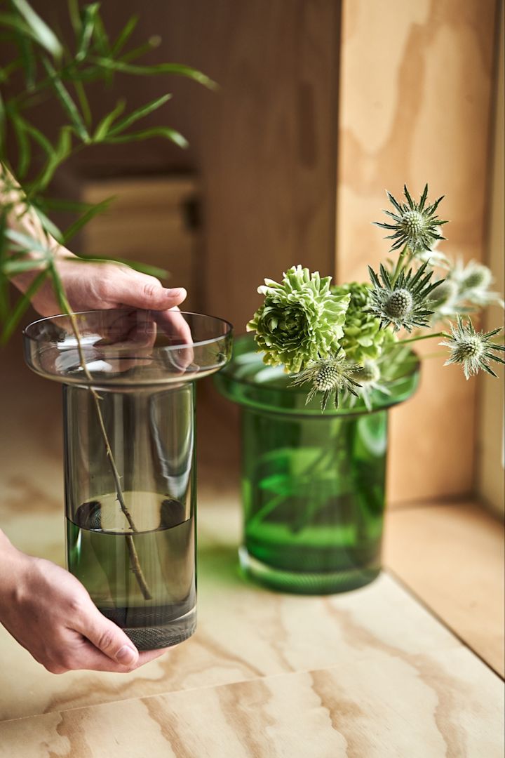 Eine Hand platziert eine graue Vase aus der Limelight-Kollektion von Kosta Boda auf einer Holzbank.