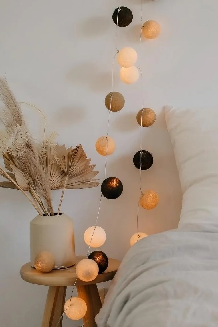 Mit ihrem beigen und braunen Farbtönen ist die Lichterkette Biscotti von Irislights, hier neben einem Bett hängend, die perfekte Boho Deko.