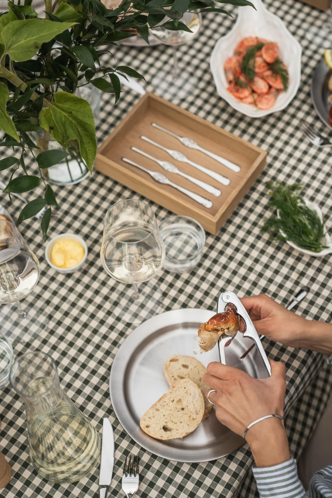 Mit dem Meeresfrüchte-Set von Hardanger können Sie die Krebse während der Kräftskiva ganz einfach knacken. Hier sitzt eine Person an einem sommerlich gedeckten Tisch und öffnet eine Krebsschere mit der Zange.