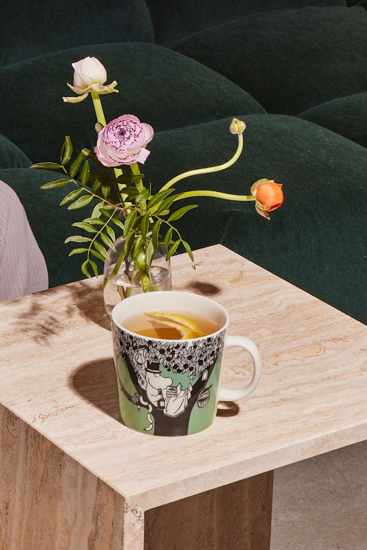 Die grüne Mumin-Tasse steht mit Kaffee auf einem Couchtisch.