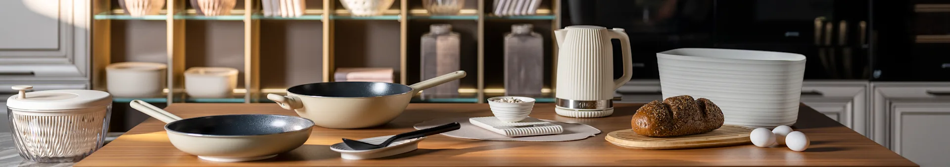 Küchentheke mit beigen Pfannen, einem weißen geriffelten Wasserkocher, einem Körnerbrot auf einem Brett und Eiern. Moderne Küchenaccessoires.