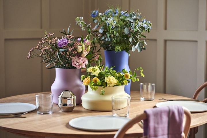 Hier sehen Sie die farbenfrohen Keramik-Vasen aus der neuen Dorotea-Kollektion auf einem gedeckten Esstisch stehend und mit bunten Blumen bestückt.