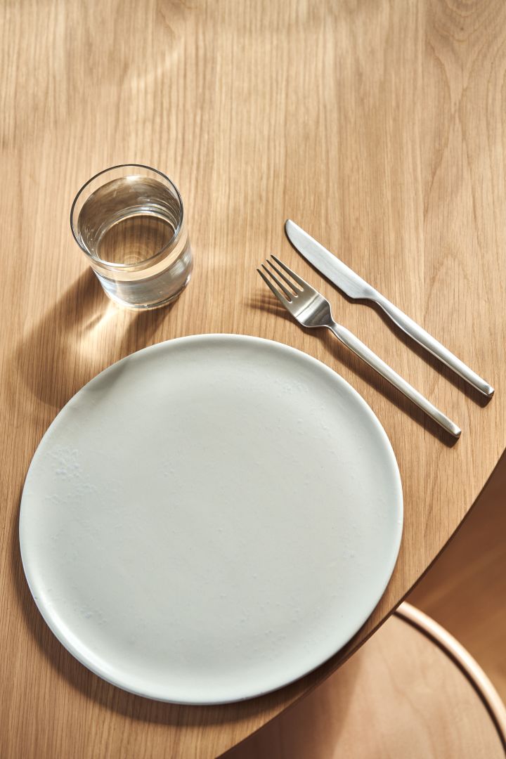 Eine Draufsicht auf das Dorotea-Besteck von Gense in Kombination mit einem schlichten weißen Teller auf einem Holztisch.