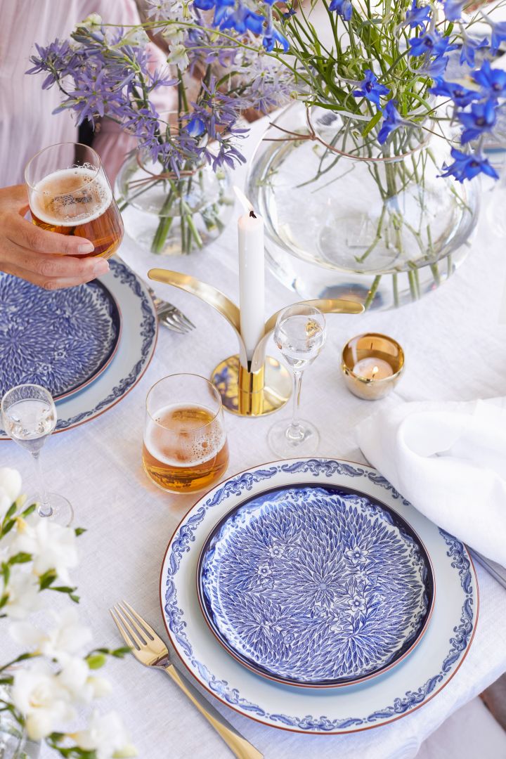 Decken Sie den Tisch für den Hochsommer in klassischem Blau und Weiß mit Tellern aus den Serien Ostindia und Ostindia Floris von Rörstrand, kombiniert mit Messingdetails. 
