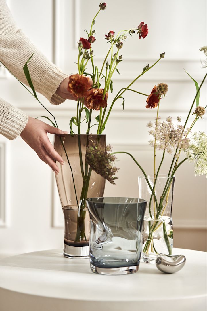 Eine runde weiße Vase mit einigen kurzen Blumen darin auf einem Regal aus Holz.