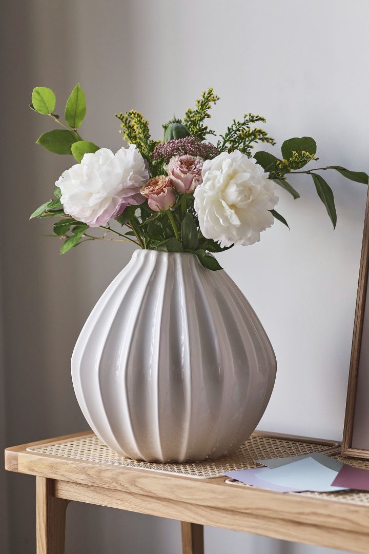 Eine runde weiße Vase mit einigen kurzen Blumen darin auf einem Regal aus Holz.