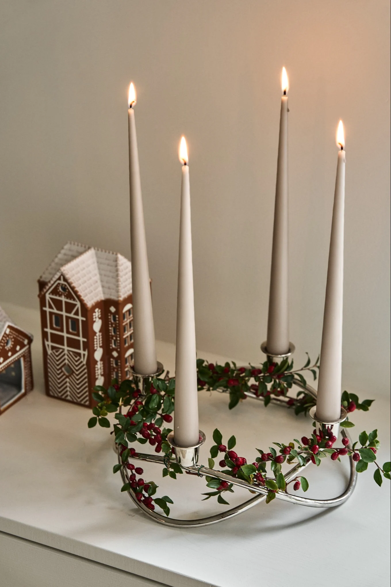 Moderne Weihnachtsdeko – hier sehen Sie den saisonalen Adventskerzenhalter von Georg Jensen aus Chrom, verziert mit grünen Blättern und roten Beeren für Weihnachten. 