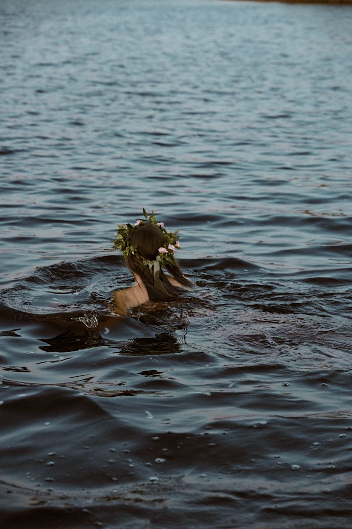 Summer Bucket List: Hier schwimmt eine Frau mit einem Mittsommerkranz im Meer.