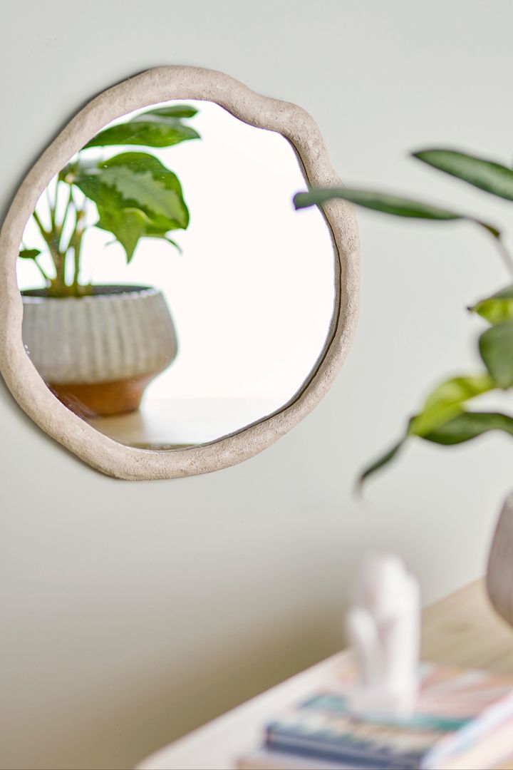 Boho Deko: Der Cillia Spiegel von Bloomingville hängt an einer Wand, davor steht eine Pflanze im Topf.