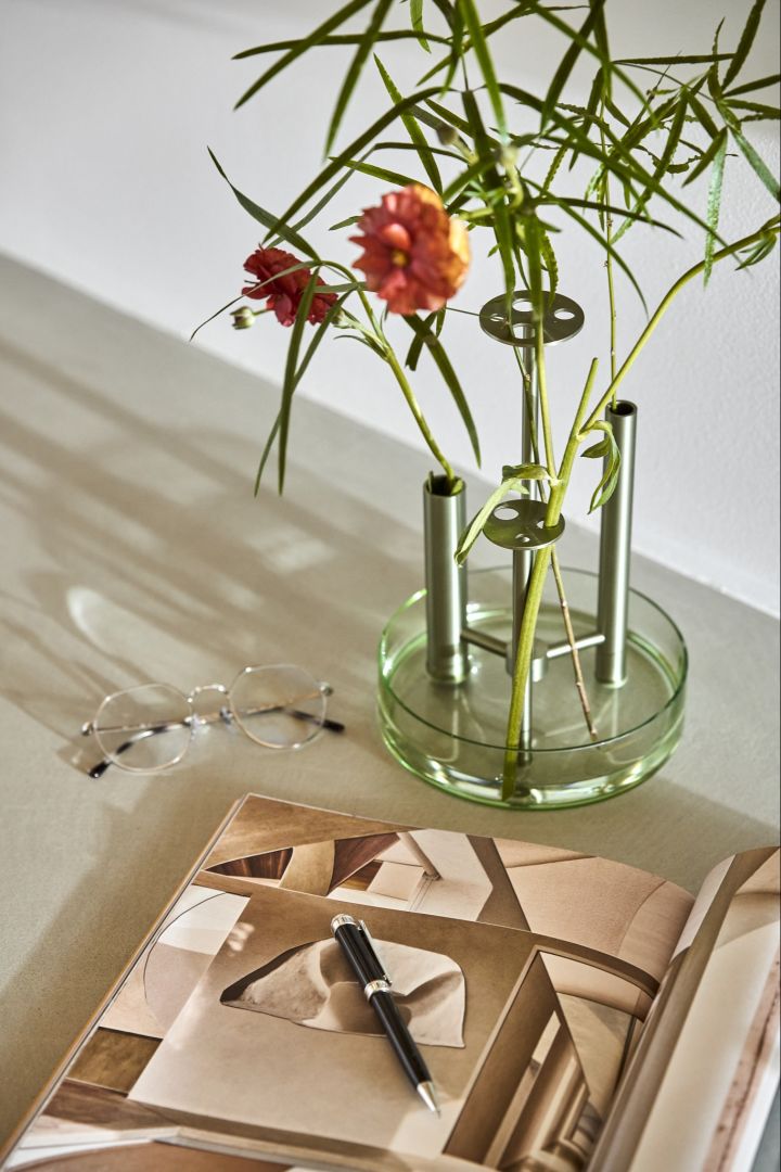 Hier sehen Sie die Ikeru Vase von Fritz Hansen, versehen mit roten Blumen, neben einer Zeitschrift.