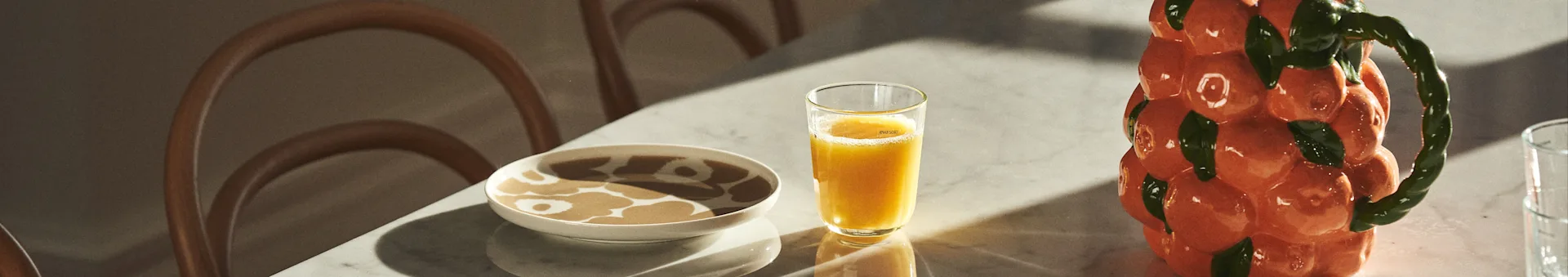 Hier sehen Sie einen gedeckten Tisch mit Marimekko-Porzellan, Saft und Karaffe von BYON im Design von Mandarinen. 