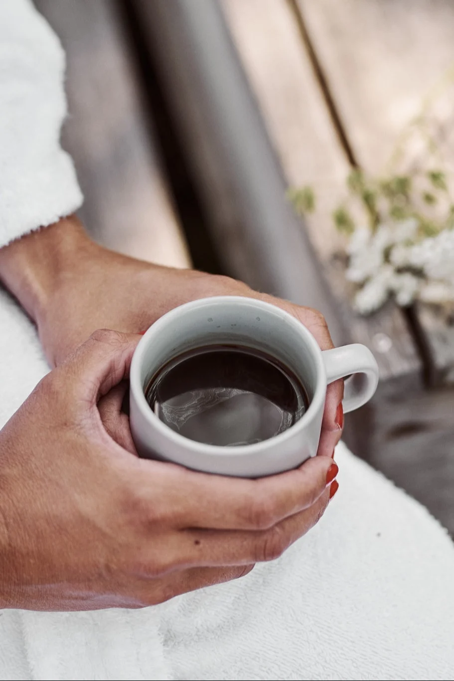 Setzen Sie eine schwedische Fika in der Sonne unbedingt auf Ihre Summer Bucket List. Hier sehen Sie Hände, die eine warme Tasse Kaffee halten.
