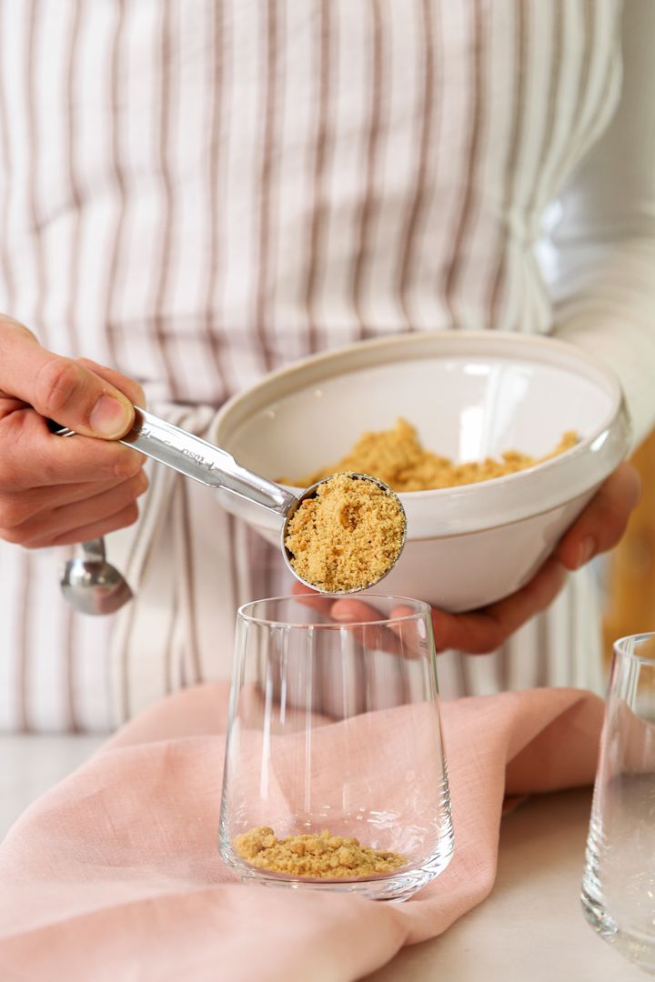 Schokodesserts für Silvester: Hier sehen Sie Frida, wie sie mit Hilfe des De Buyer-Messlöffel Sets die zerbröselten Kekse aus einer Schüssel in ein Essence-Glas von Iittala gibt.