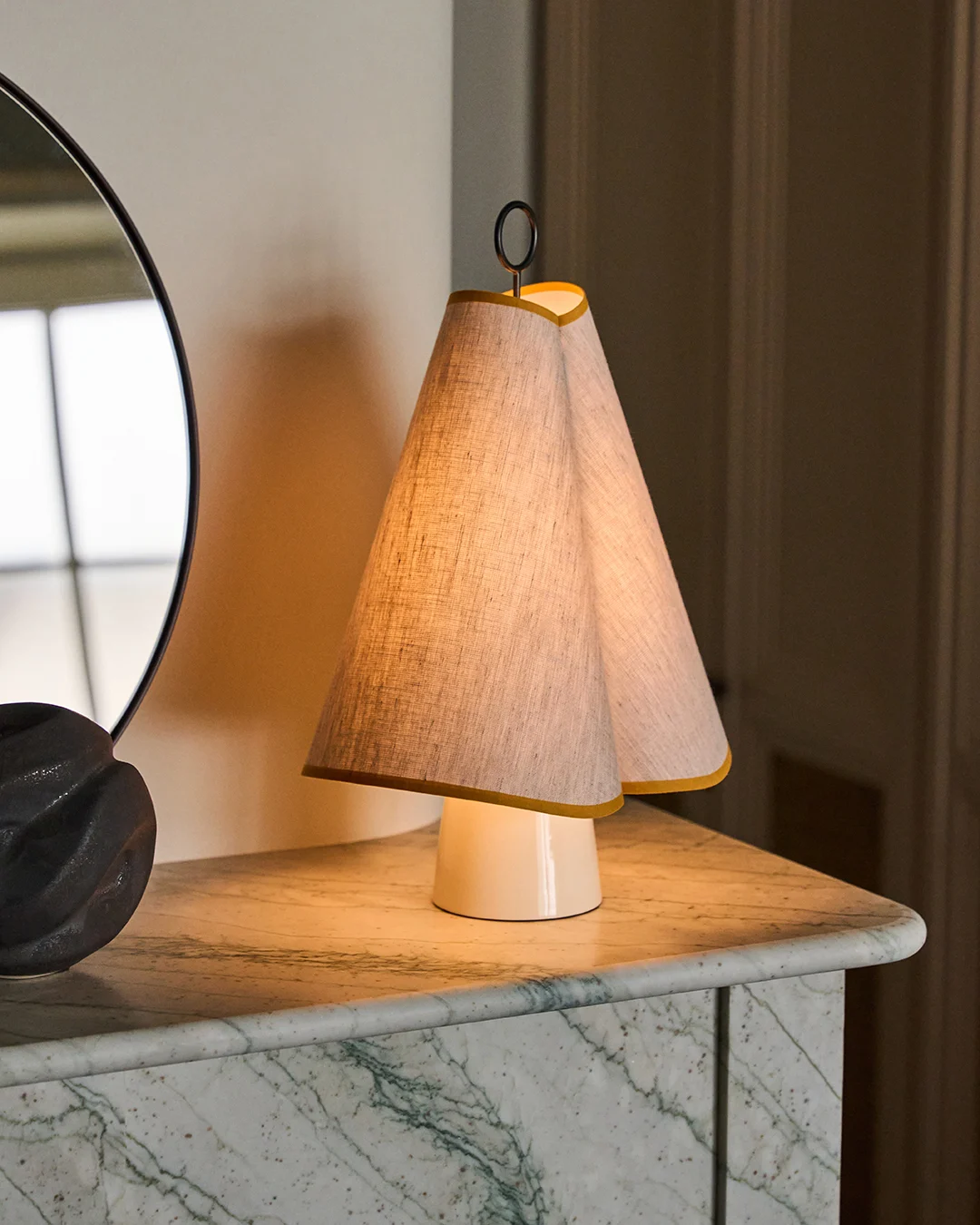 Eine einzigartige Tischlampe mit doppeltem konischem Stoffschirm, gelb eingefasst, die ein warmes Licht auf eine grüne Marmorplatte wirft.