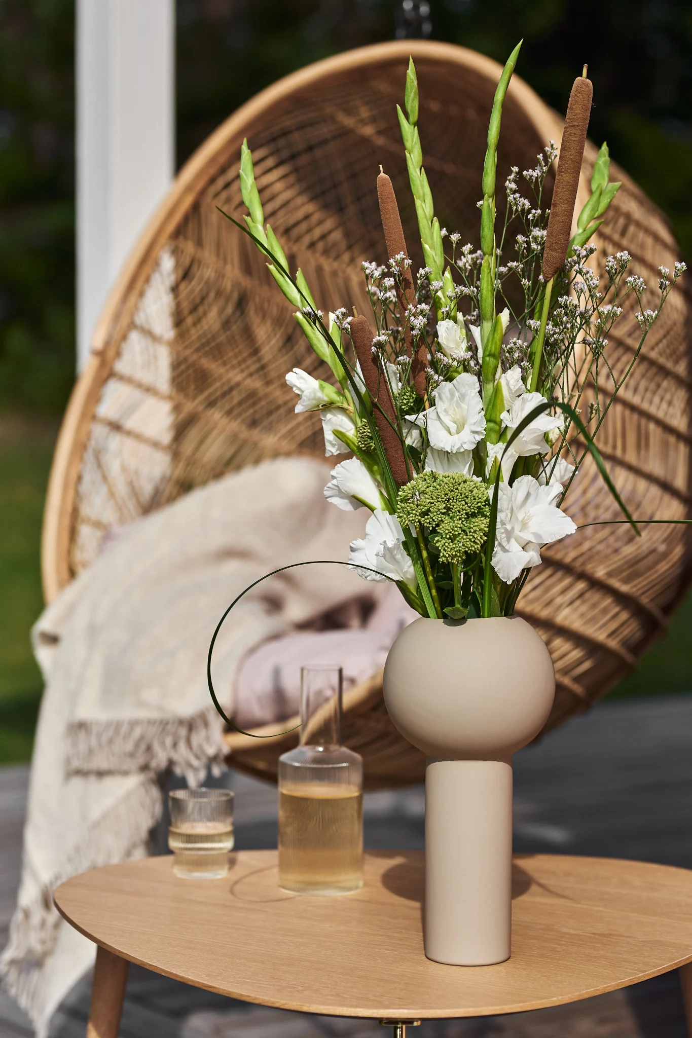 Auf einem Tisch in einem Garten steht die hohe Pillar-Vase in Beige von Cooee Design mit frisch geschnittenen Frühlingsblumen.