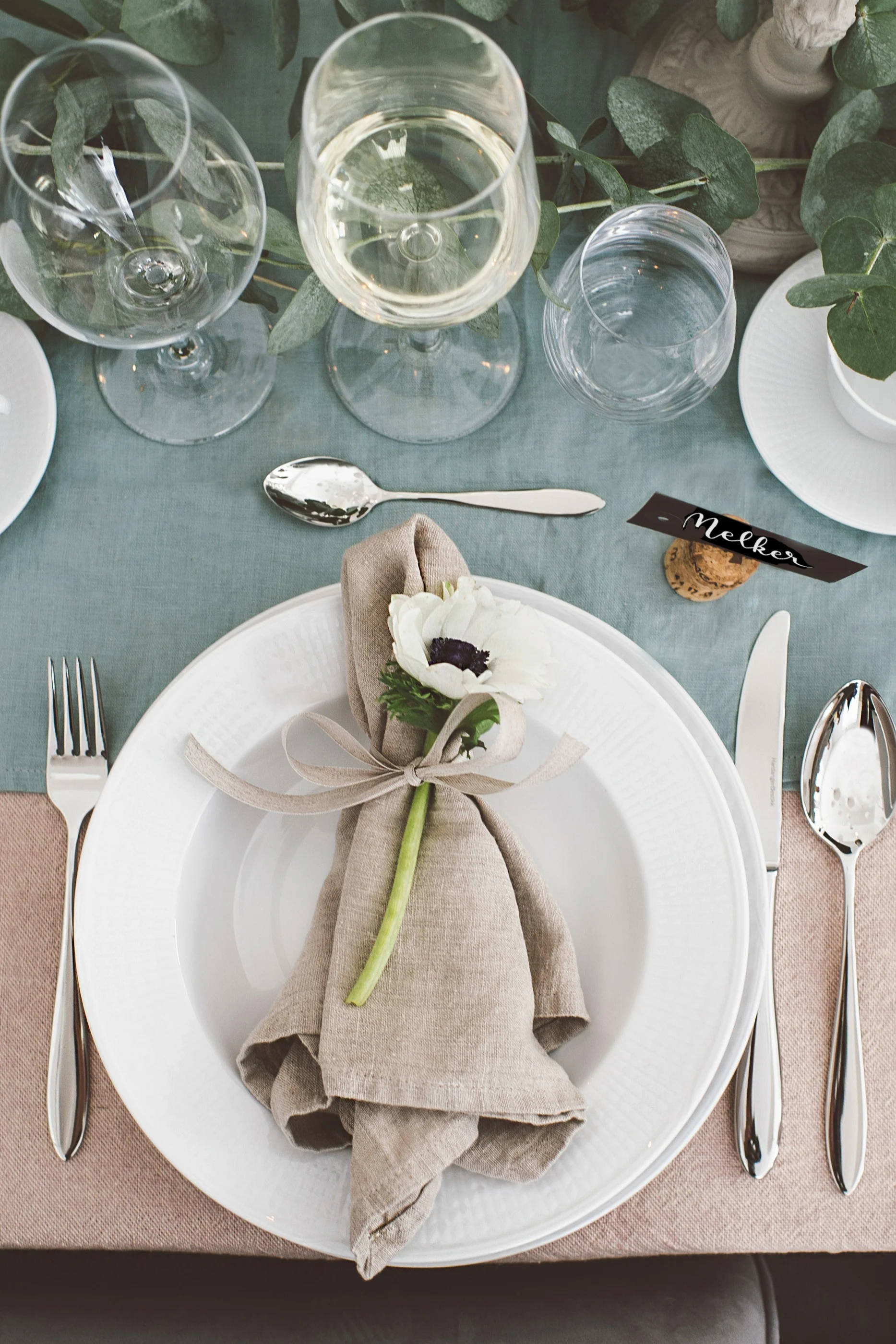 Beigefarbene Leinenserviette, gebunden mit einem dekorativen Band und einer leuchtenden Blume auf einem festlich gedeckten Tisch.
