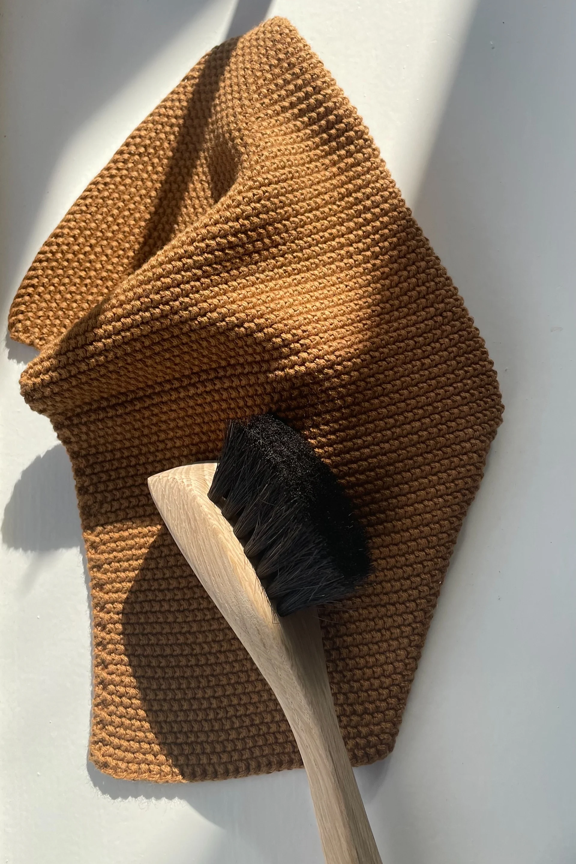 Reinigen Sie Ihre Bratpfanne mit einer Spülbürste, die hier auf einem braunen Spüllappen liegt, beides von Humdakin.