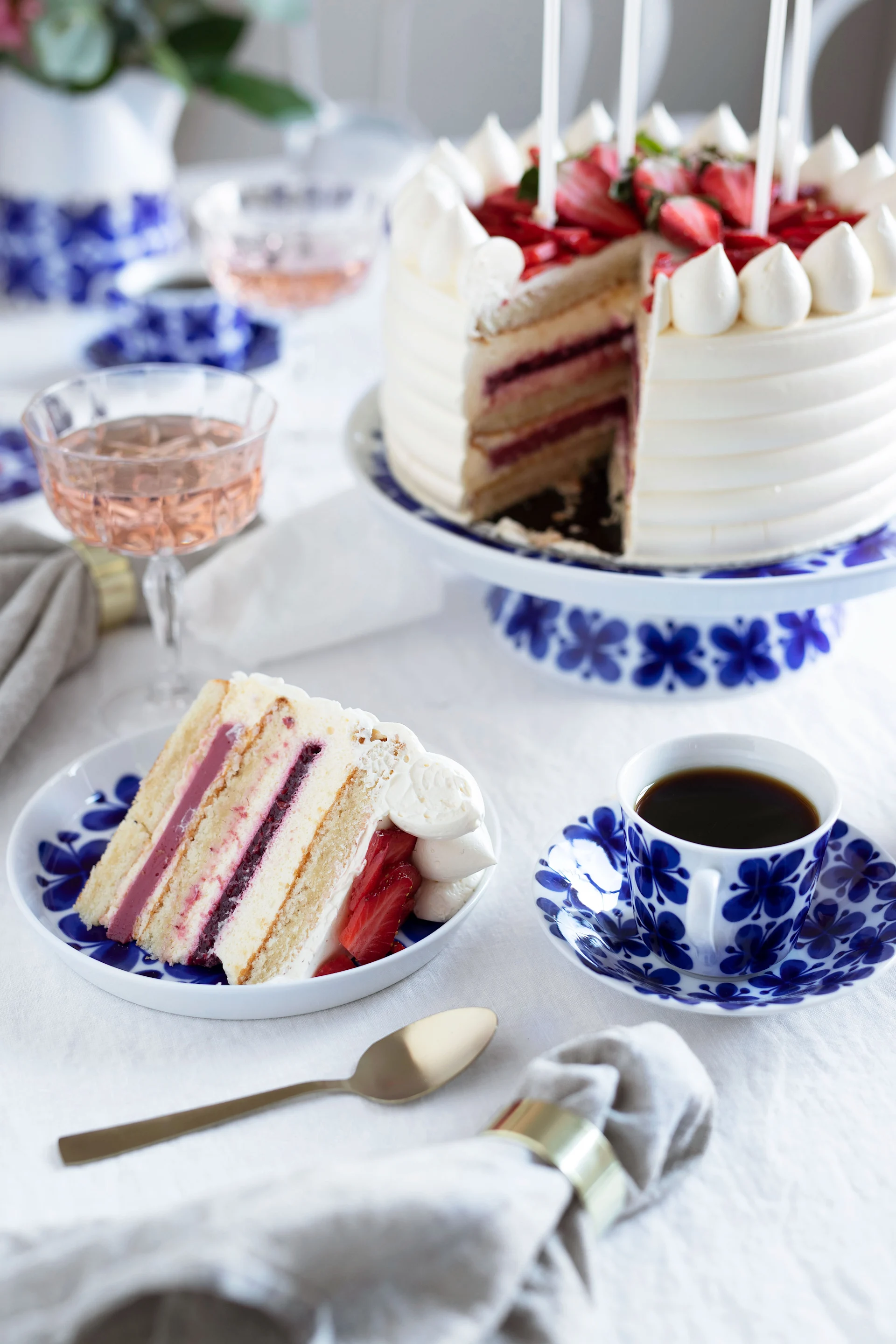 Erdbeerkuchen mit einem Stück herausgeschnitten, serviert auf blau-weiß gemustertem Geschirr mit Kaffee und Rosé.
