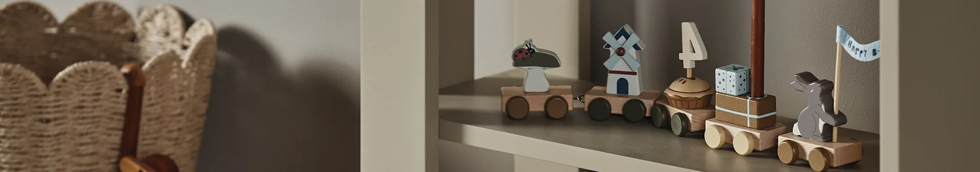 Ein Holzspielzeugzug auf einem Regal mit Waggons, die einen Marienkäfer, eine Windmühle, einen Cupcake mit "4"-Kerze, ein Geschenk und einen Hasen mit "Happy B"-Flagge zeigen.