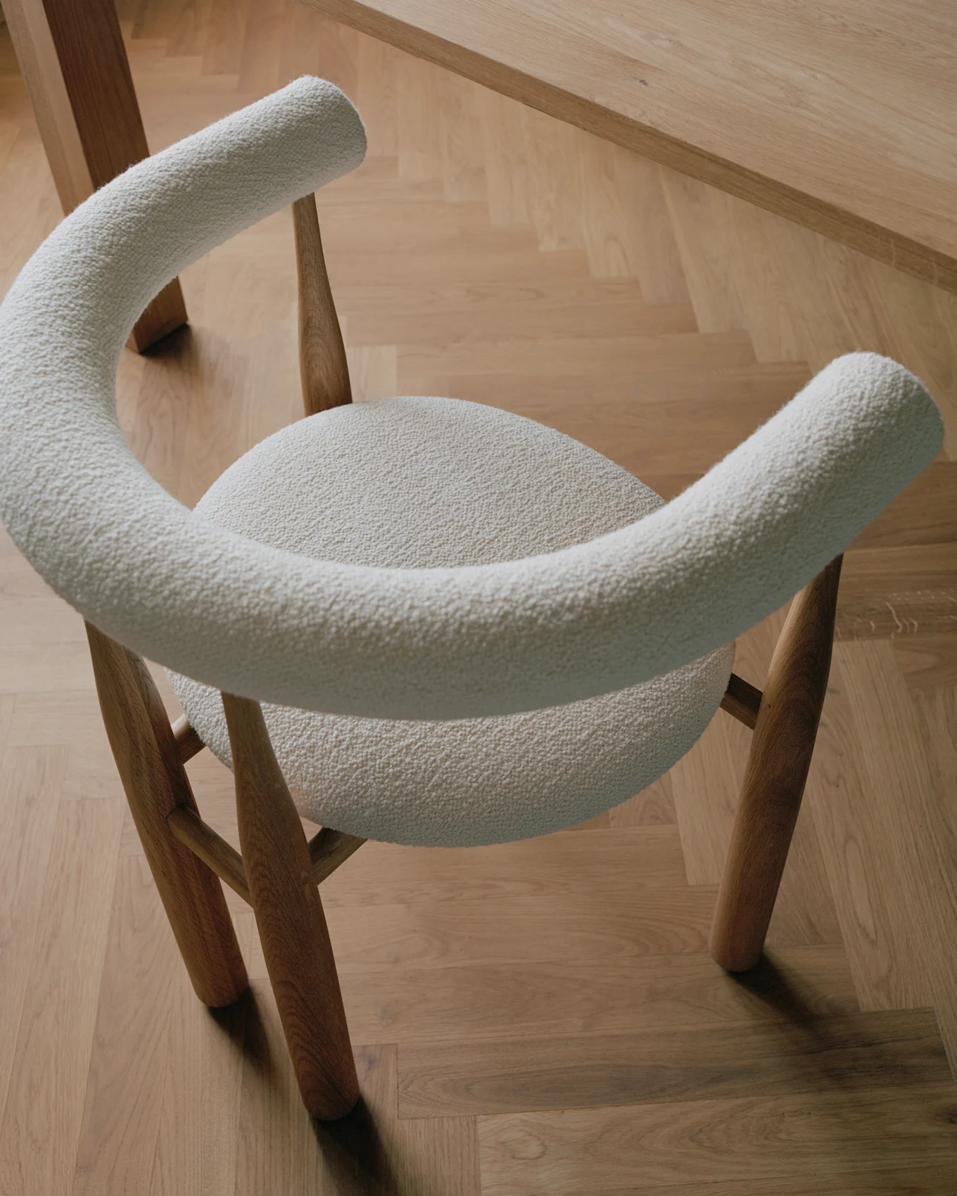 Moderner Stuhl mit hellem Bouclé-Stoffbezug und Holzbeinen auf hellem Holzparkettboden.